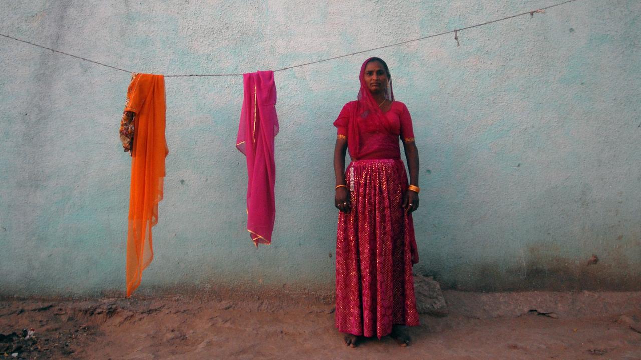 Eine junge indische Frau steht vor einer Wand in einem rosafarbenen Sari.
