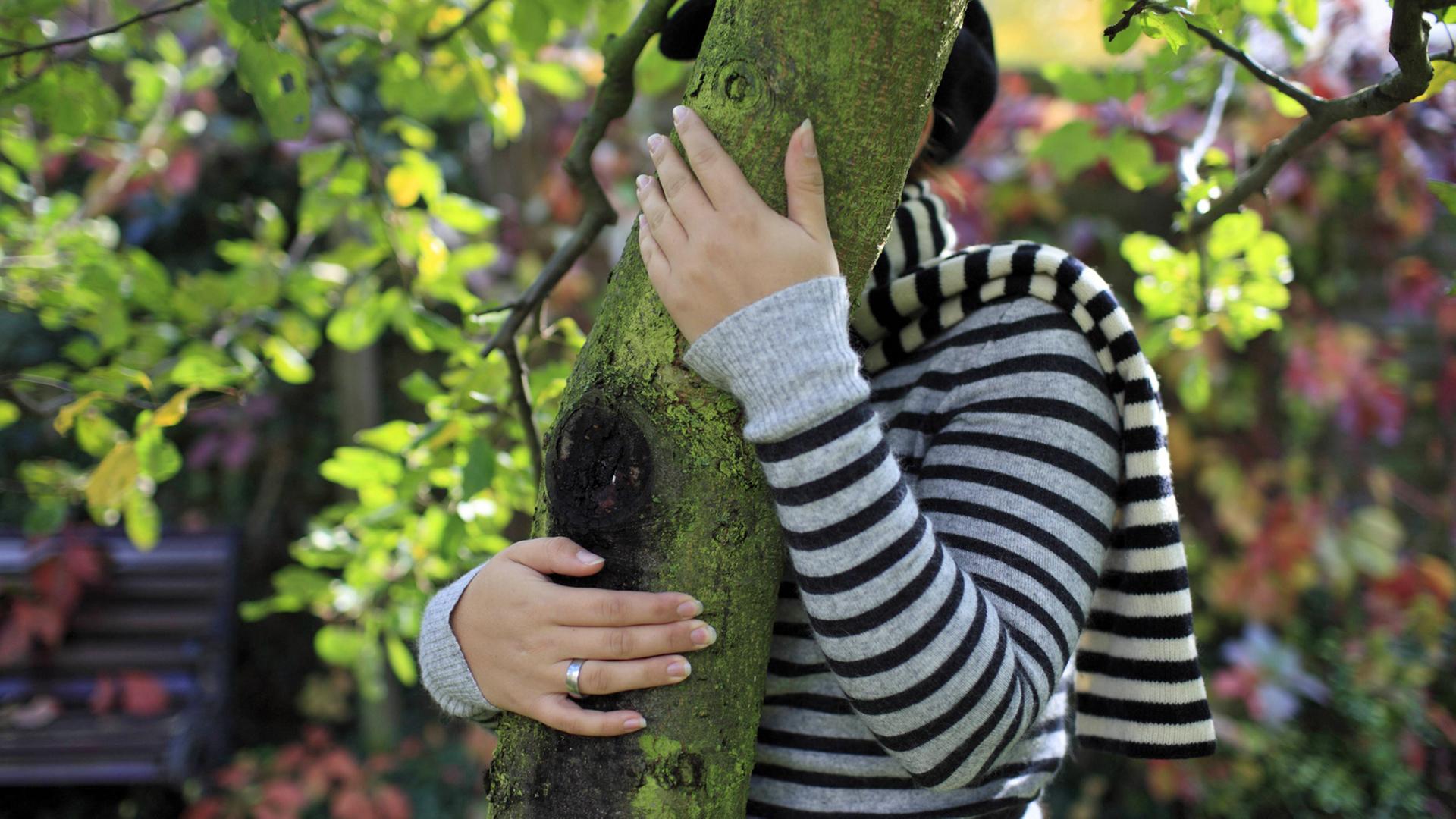 Eine junge Frau versteckt sich hinter einem Baumstamm. Eine junge Frau versteckt sich hinter einem Baumstamm.