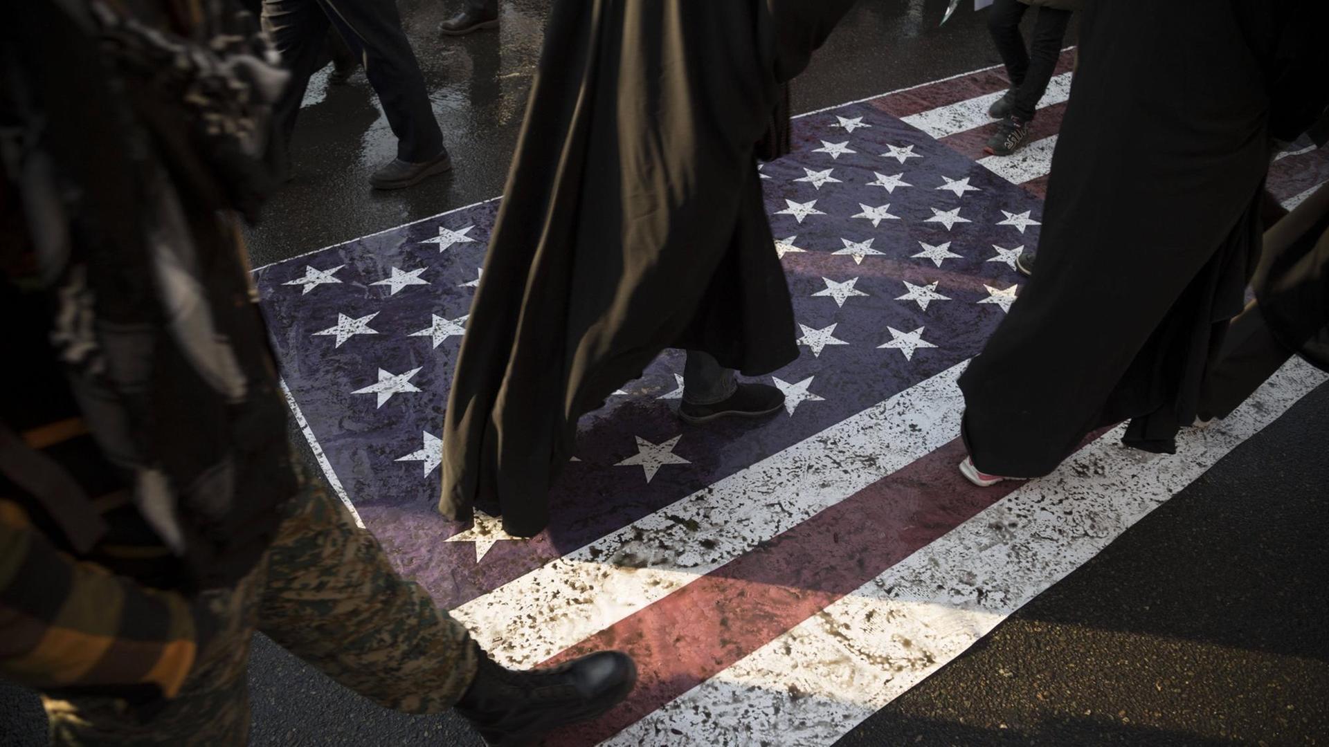 Menschen laufen während einer Trauerfeier in der iranischen Hauptstadt Teheran über eine amerikanische Flagge Menschen laufen während einer Trauerfeier in der iranischen Hauptstadt Teheran über eine amerikanische Flagge