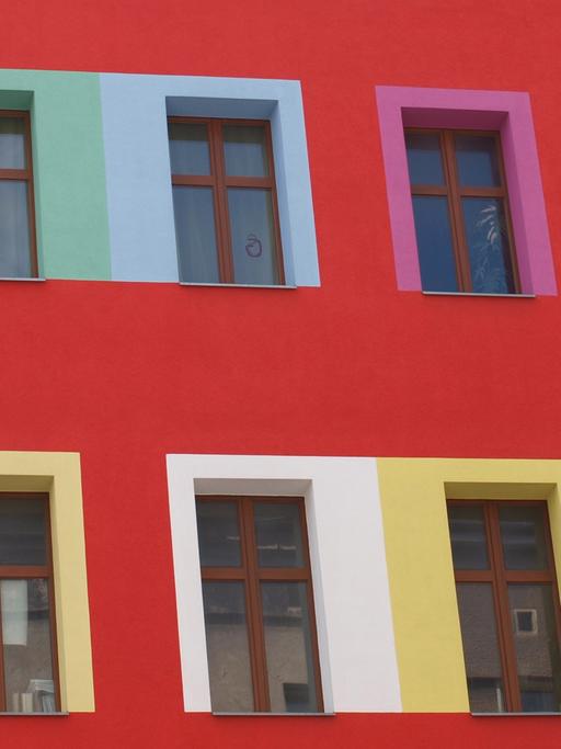Blick auf die Fassade eines Mehrfamilienhauses mit bunten Fensterrahmen.
