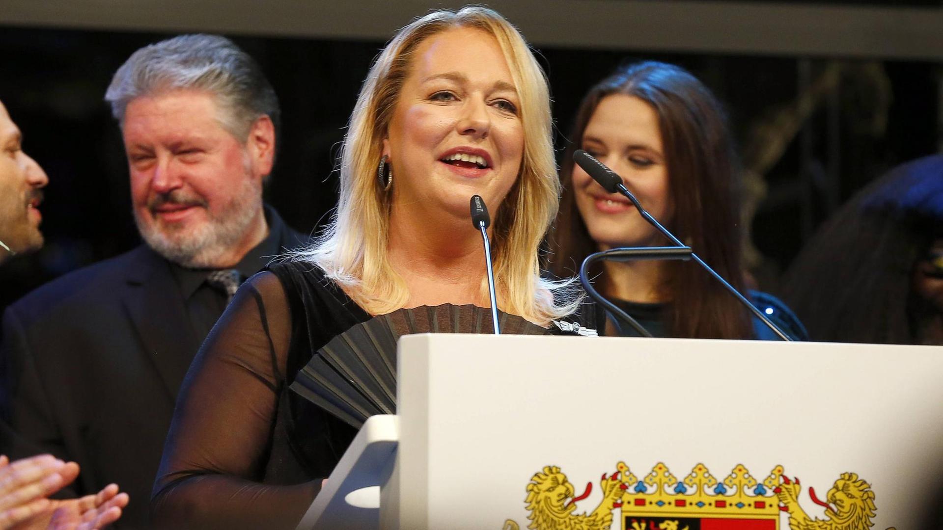 Festspielleiterin Katharina Wagner spricht hinter einem Pult mit den Wappen von Bayreuth in Mikrofone.
