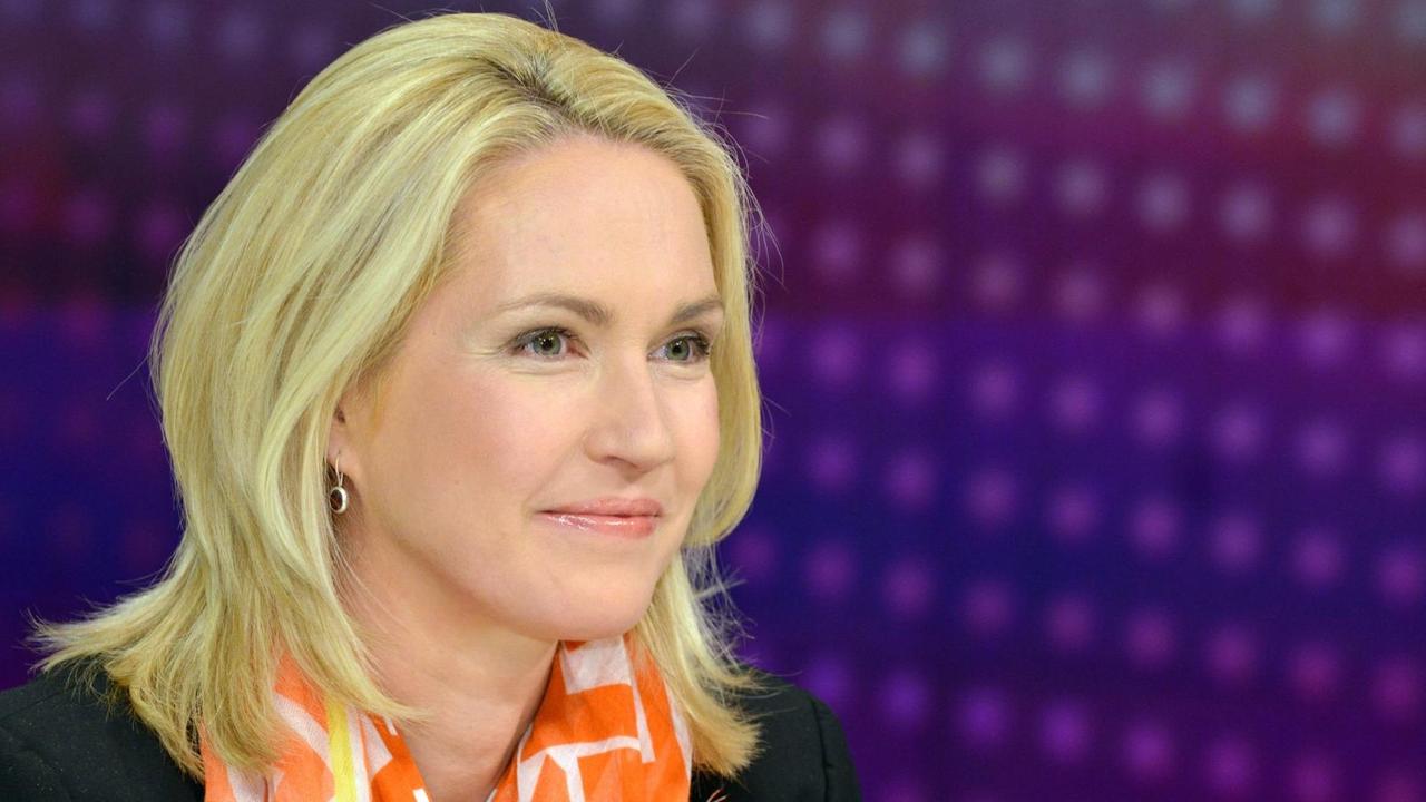 Schwesig sitzt lächelnd und mit orange-weißem Halstuch vor einem liafarbenen Hintergrund. Schwesig sitzt lächelnd und mit orange-weißem Halstuch vor einem liafarbenen Hintergrund.