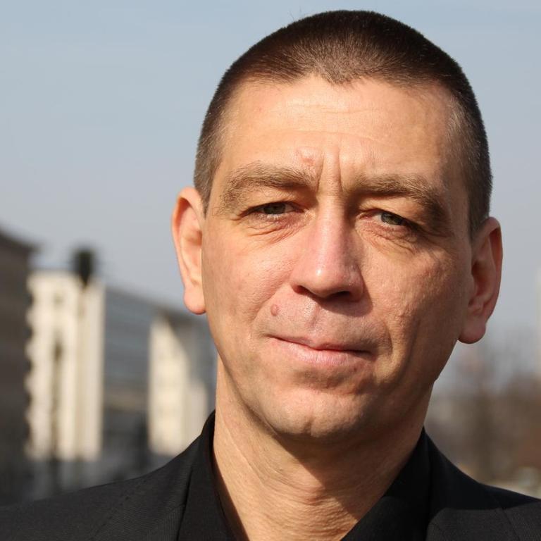 Historiker Jens Schöne ist stellvertretender Berliner Beauftragter zur Aufarbeitung der SED-Diktatur. Er steht draußen, in schwarzem Anzug mit kurzen Haaren.
