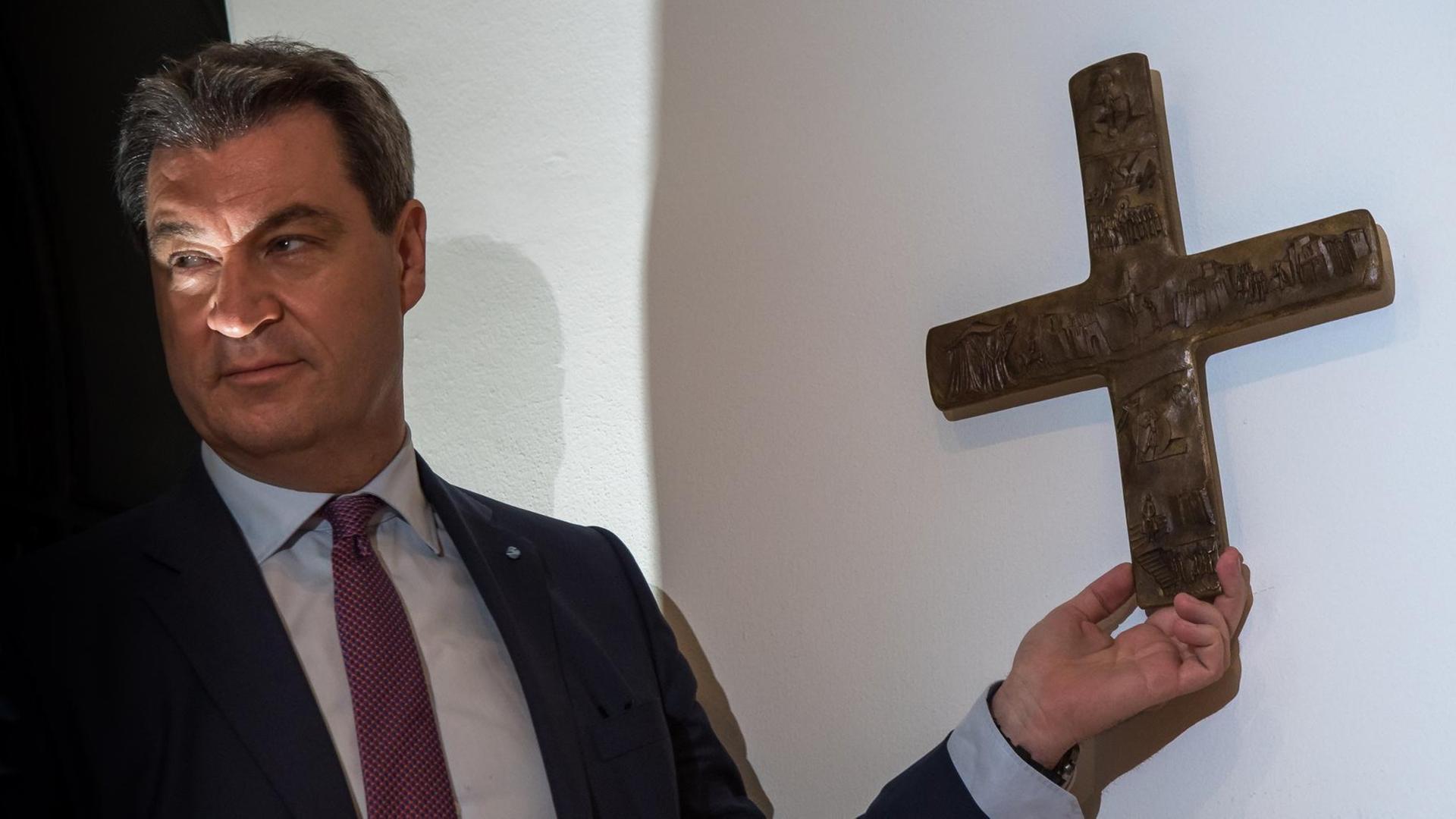 Bayerns Ministerpräsident Söder bringt nach dem Beschluss des Landeskabinetts zur Aufhängung von Kreuzen ein erstes Exemplar in der Staatskanzlei an. Bayerns Ministerpräsident Söder bringt nach dem Beschluss des Landeskabinetts zur Aufhängung von Kreuzen ein erstes Exemplar in der Staatskanzlei an.