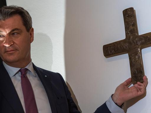 Bayerns Ministerpräsident Söder bringt nach dem Beschluss des Landeskabinetts zur Aufhängung von Kreuzen ein erstes Exemplar in der Staatskanzlei an.
