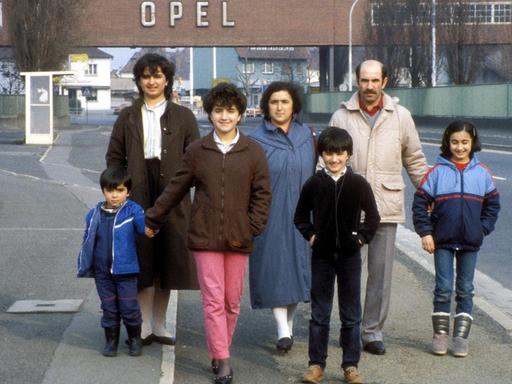 Eine türkische Gastarbeiterfamilie steht vor dem Tor der Opel-Werke in Rüsselsheim im Jahr 1984.