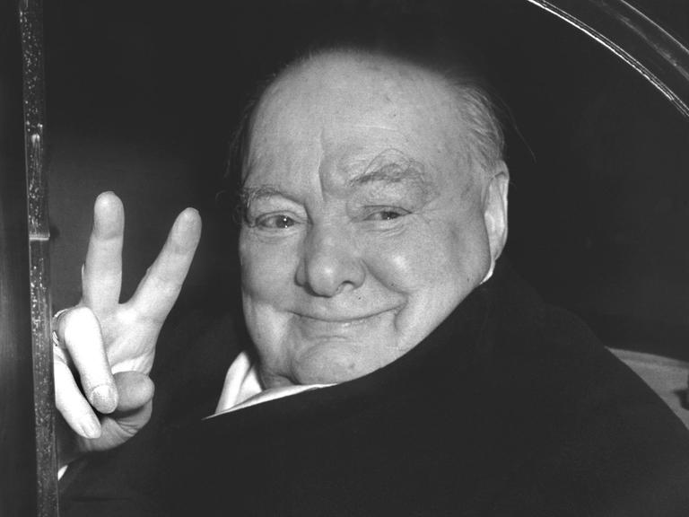 Der britische Staatsmann Sir Winston Churchill (1874-1965) grüßt aus einem Fahrzeug heraus mit der für ihn typischen Geste, dem Victory-Zeichen.