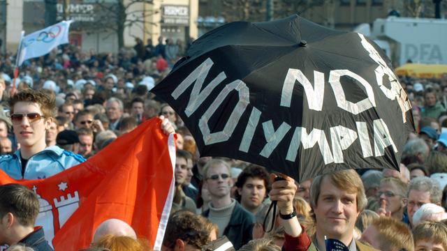 "No Olympia" steht auf dem Schirm, den ein Mann auf dem Rathausplatz in Hamburg am 12.04.2003 in die Höhe hält.