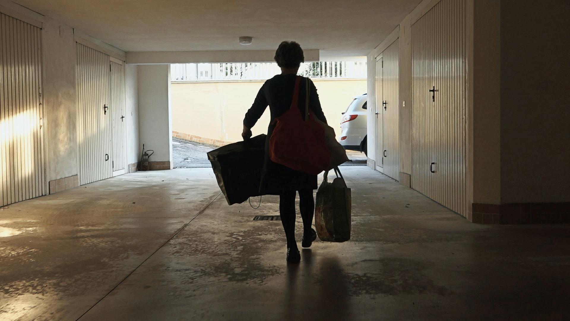 Rückansicht einer Frau, die mit mehreren Taschen Richtung eines Ausgangs geht. Rückansicht einer Frau, die mit mehreren Taschen Richtung eines Ausgangs geht.
