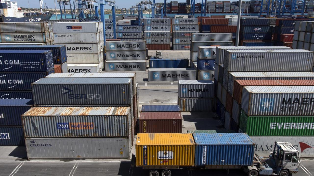 Das Bild zeigt viele übereinandergestapelte Containertürme, die meisten mit der Aufschrift "Maersk". Im Hintergrund Kräne und ein Hafenbecken. Das Bild zeigt viele übereinandergestapelte Containertürme, die meisten mit der Aufschrift "Maersk". Im Hintergrund Kräne und ein Hafenbecken.