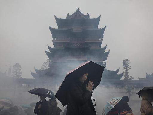 Eine Frau mit einem Regenschirm betet vor der Silhouette eines buddhistischen Tempels.