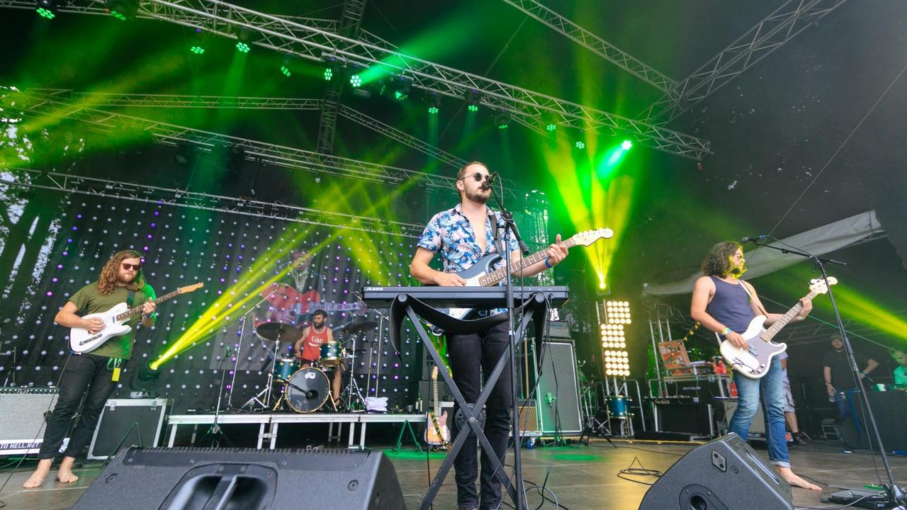 Vier Musiker an Gitarre, Schlagzeug, Keyboard und Bass stehen auf einer Bühne. Scheinwerfer verteilen grünes Licht. Vier Musiker an Gitarre, Schlagzeug, Keyboard und Bass stehen auf einer Bühne. Scheinwerfer verteilen grünes Licht.