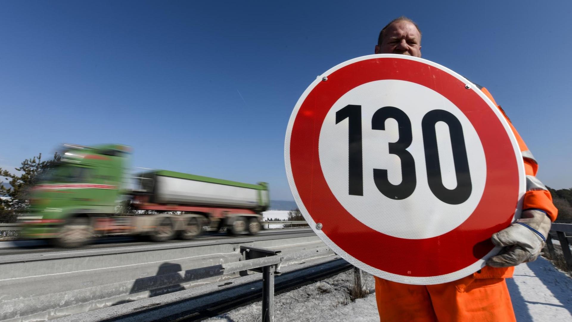 Ein Straßenwärter hält an der Autobahn A81 am Hegaublick ein Schild mit der Aufschrift "130" in den Händen