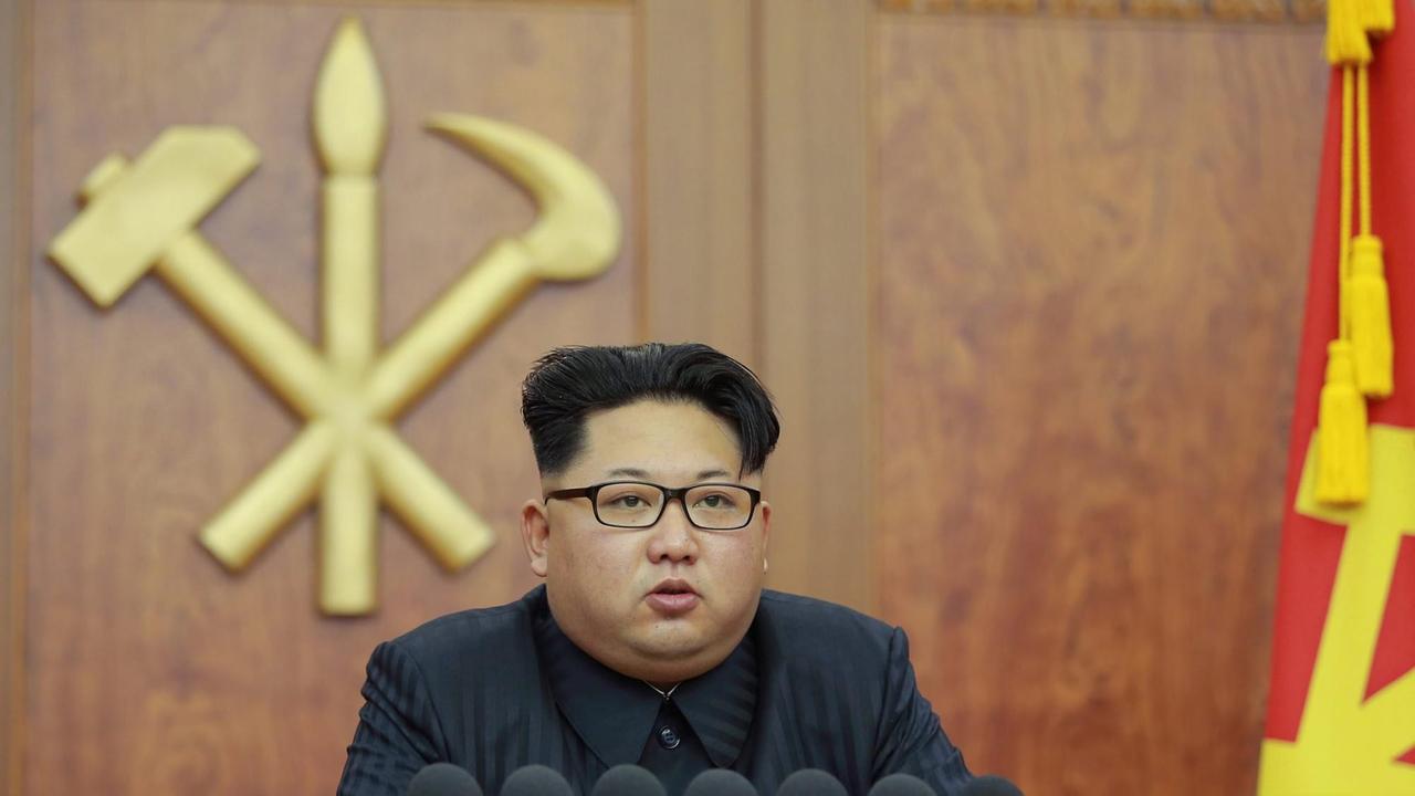 Zu sehen ist Nordkoreas Machthaber Kim Jong Un am Schreibtisch mit Brille, dahinter die Symbole Hammer, Sichel und Pinsel an einer Holzwand. Zu sehen ist Nordkoreas Machthaber Kim Jong Un am Schreibtisch mit Brille, dahinter die Symbole Hammer, Sichel und Pinsel an einer Holzwand.