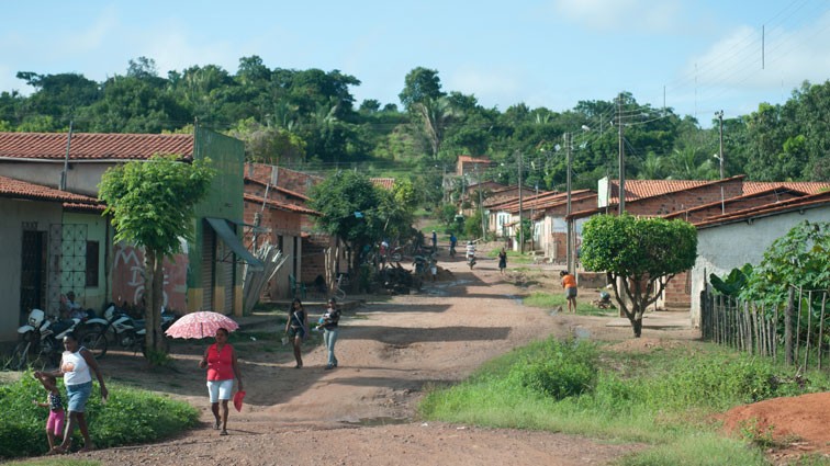 Eine Frau mit Sonnenschirm läuft auf der ungeteerten Straße eines Dorfes in Codó im Norden Brasiliens, rechts und links der Straße stehen kleine Häuser. Eine Frau mit Sonnenschirm läuft auf der ungeteerten Straße eines Dorfes in Codó im Norden Brasiliens, rechts und links der Straße stehen kleine Häuser.