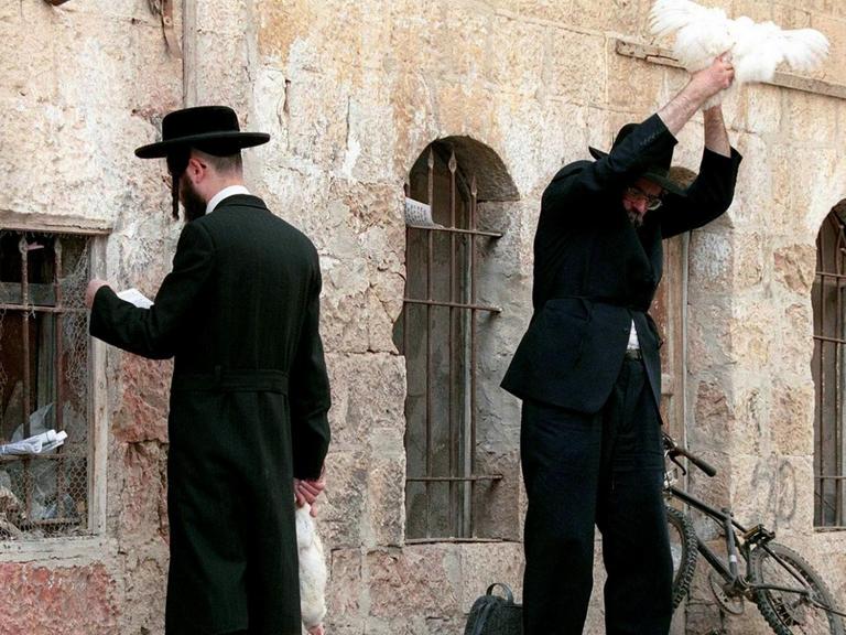 Zwei orthodoxe Juden im Jerusalemer Viertel Mea Shearim: Einer betet gegen eine Mauer, der andere schwingt ein Huhn über seinem Kopf