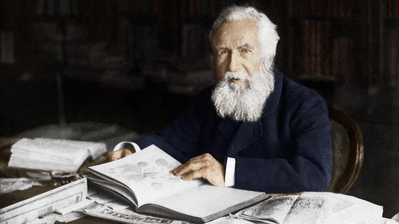 Ein digital koloriertes Schwarz-Weiß-Foto zeigt Ernst Haeckel an seinem Schreibtisch. Ein digital koloriertes Schwarz-Weiß-Foto zeigt Ernst Haeckel an seinem Schreibtisch.
