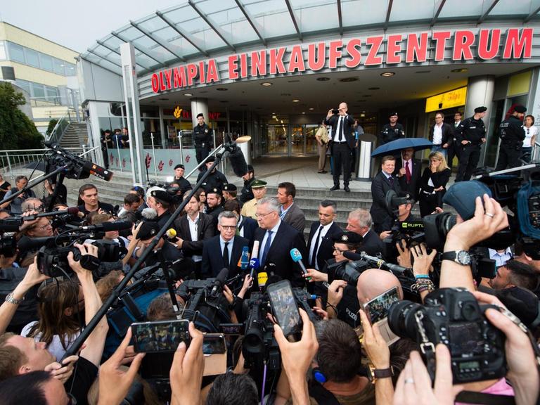 Bundesinnenminister Thomas de Maiziere (CDU, Mitte, l) und Bayerns Innenminister Joachim Herrmann (CSU, Mitte, r) geben einen Tag nach einer Schießerei mit Toten und Verletzten, vor dem Olympia-Einkaufszentrum (OEZ) in München (Bayern) ein Statement ab.