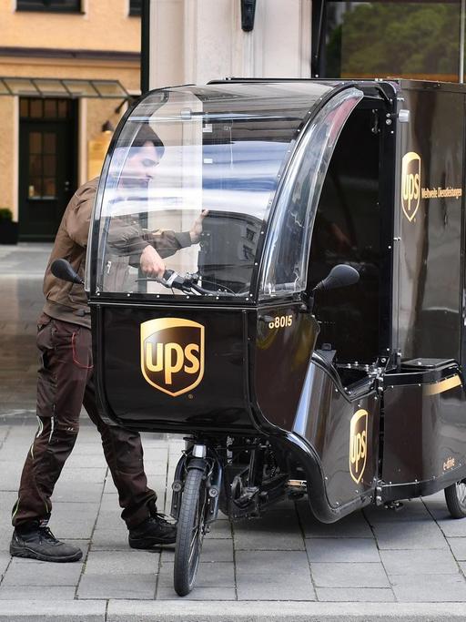 Ein Paketzusteller der Firma UPS steht auf der Straße neben seinem Lastenrad.