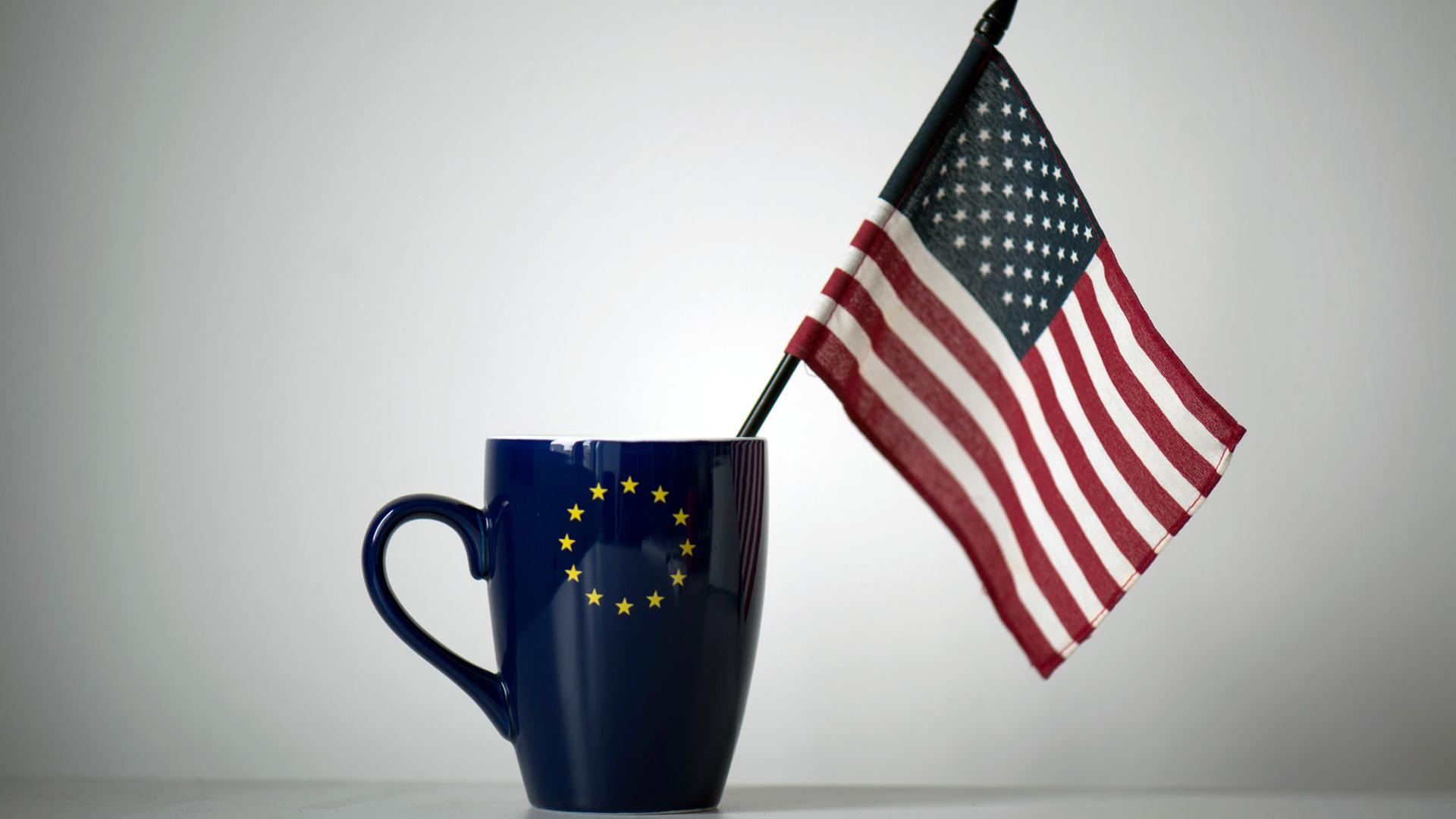 In einer Tasse mit einem EU-Symbol steckt eine US-Fahne. In einer Tasse mit einem EU-Symbol steckt eine US-Fahne.