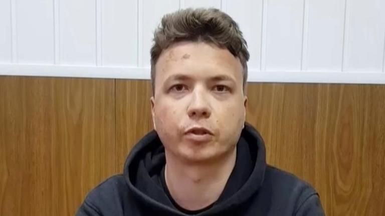 Man sieht den Torso von Roman Protasewitsch vor einer holzgetäfelten Wand. Er trägt einen Kapuzenpulli und blickt ernst in die Kamera. Auf seinem Gesicht sind mehrere graue Flecken erkennbar. Man sieht den Torso von Roman Protasewitsch vor einer holzgetäfelten Wand. Er trägt einen Kapuzenpulli und blickt ernst in die Kamera. Auf seinem Gesicht sind mehrere graue Flecken erkennbar.