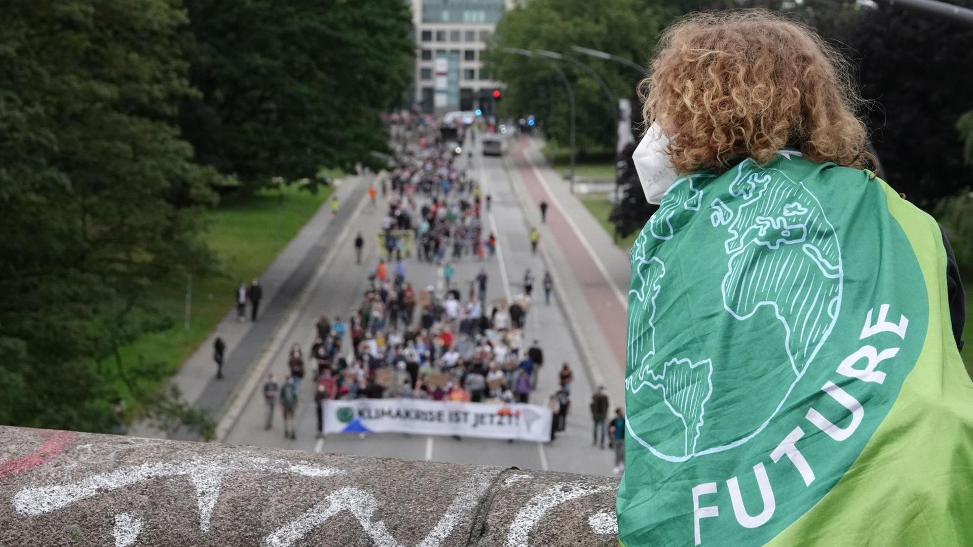 Ein Mensch mit einer Fahne mit dem Logo von Fridays for Future verfolgt von einer Brücke aus die Demonstration des Bündnisses Fridays for Future entlang einer Straße. Ein Mensch mit einer Fahne mit dem Logo von Fridays for Future verfolgt von einer Brücke aus die Demonstration des Bündnisses Fridays for Future entlang einer Straße.