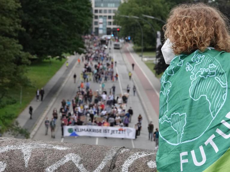 Ein Mensch mit einer Fahne mit dem Logo von Fridays for Future verfolgt von einer Brücke aus die Demonstration des Bündnisses Fridays for Future entlang einer Straße.