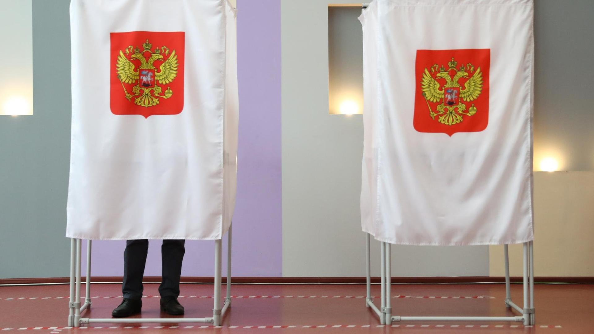 Das Bild zeigt zwei Wahlkabinen während der Parlamentswahl in Russland. In der linken steht ein Mann, es sind seine Beine unter dem Vorhang zu sehen.