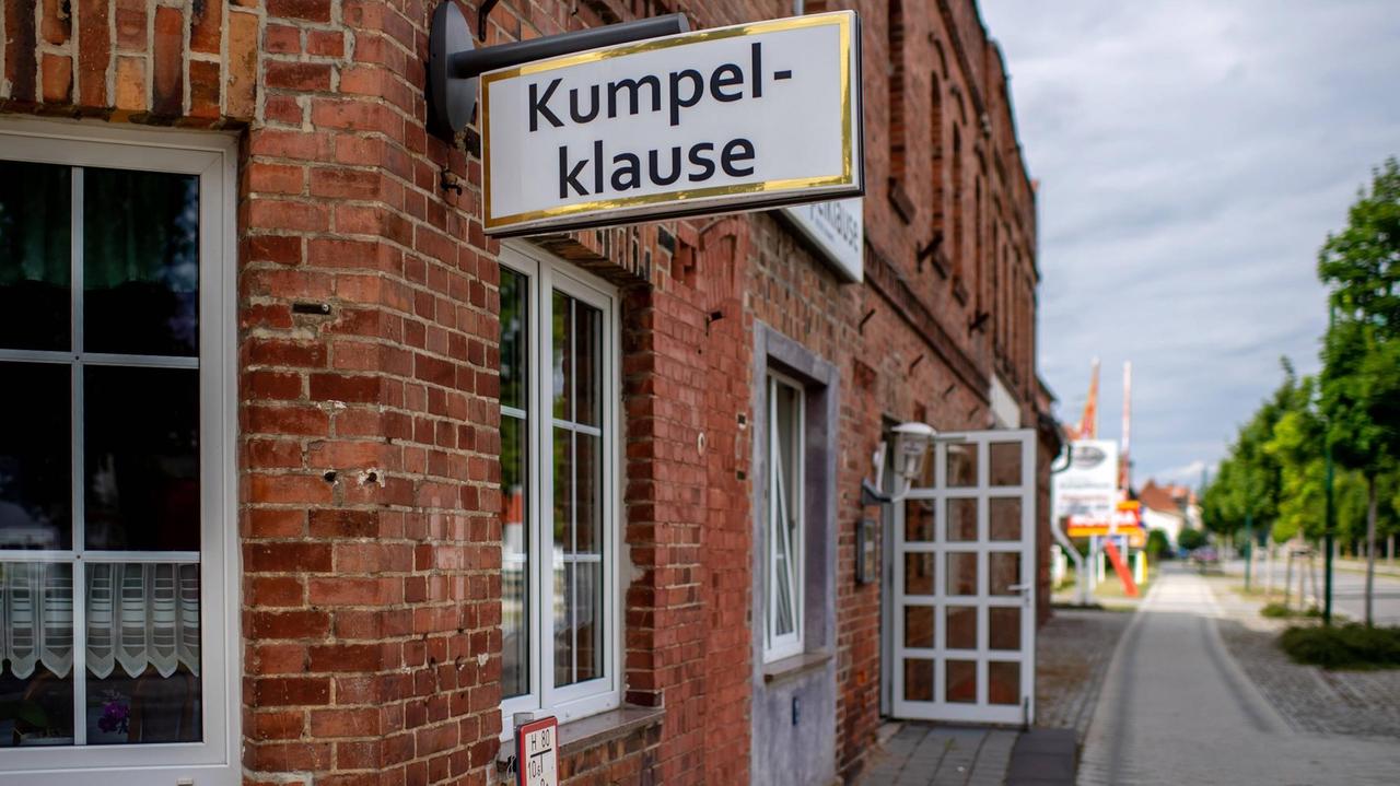 "Kumpel-Klause" steht an einem Haus aus Ziegelsteinen. Die Tür steht offen. Am rechten Bildrand verläuft die Dorfstraße in die Ferne. "Kumpel-Klause" steht an einem Haus aus Ziegelsteinen. Die Tür steht offen. Am rechten Bildrand verläuft die Dorfstraße in die Ferne.