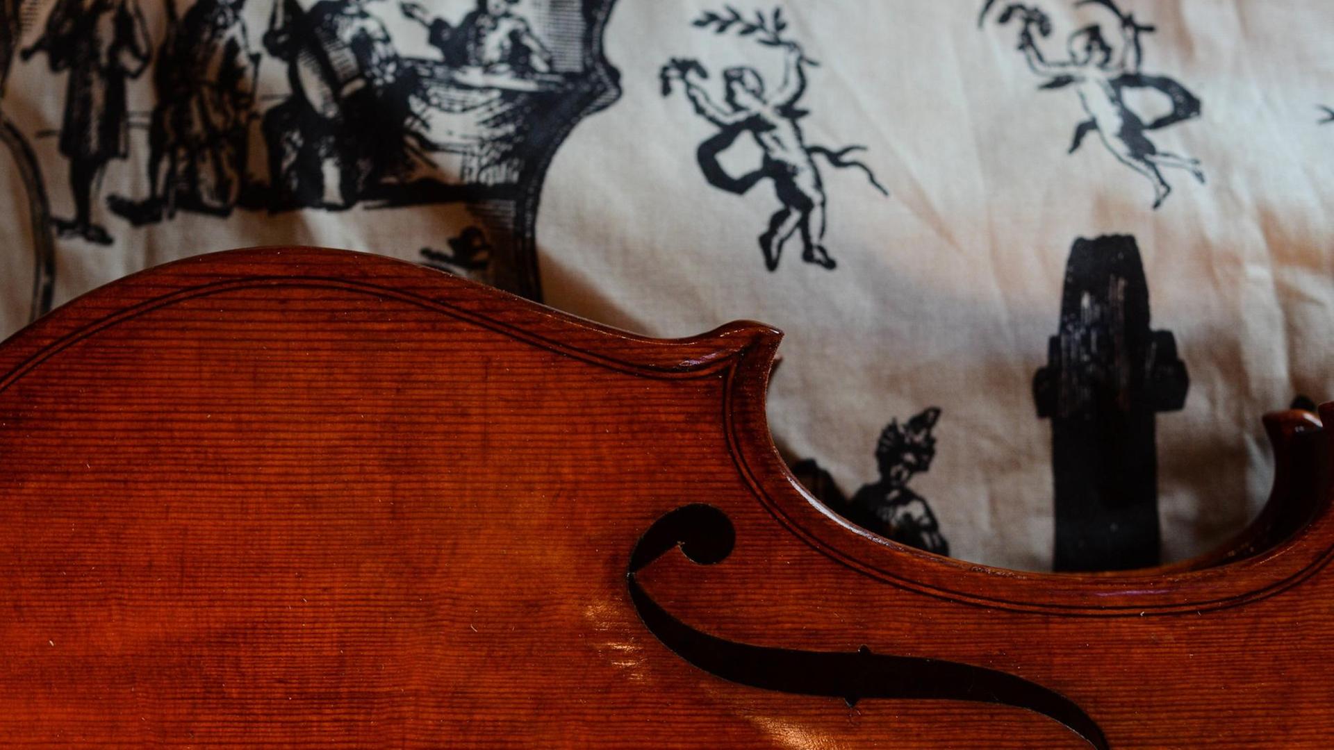Detail einer barocken Geige, die auf einem mit Putten bedrucktem Tuch liegt. Detail einer barocken Geige, die auf einem mit Putten bedrucktem Tuch liegt.