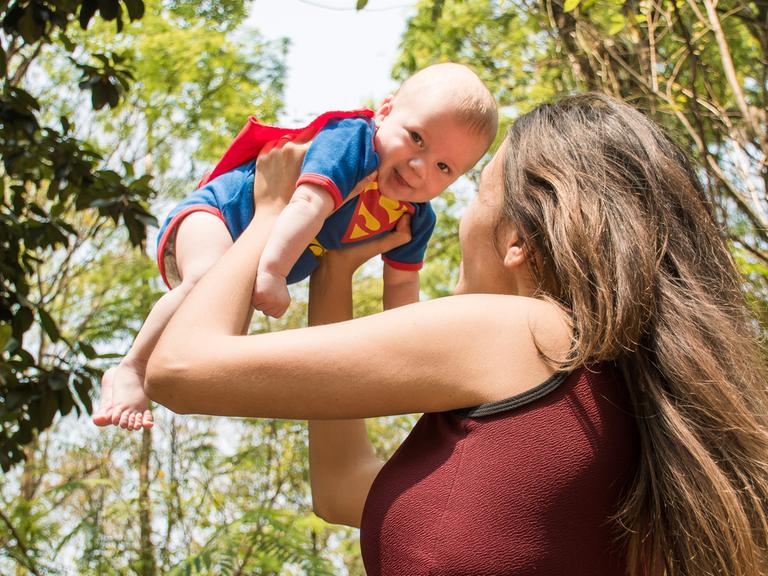 Eine Frau hebt ein Baby in einem Superman-Kostüm in die Luft.