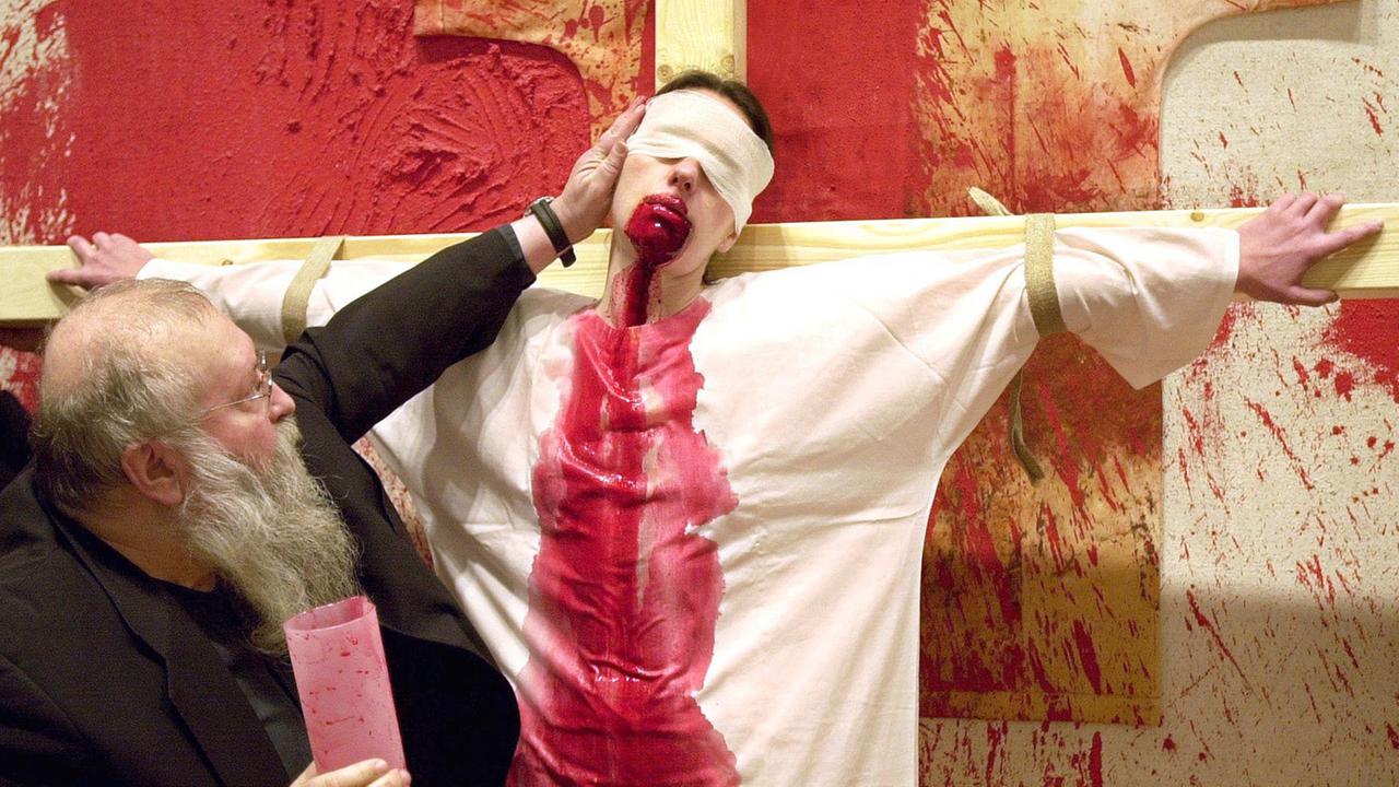 Der österreichische Künstler Hermann Nitsch rückt während einer Blut-Performance im Dezember 2001 im Frankfurter Museum Schirn den Kopf eines an ein Kreuz gebundenen Models zurecht. Aus dem Mund der Frau rinnt Schweineblut, welches ihr Nitsch zuvor eingeflößt hatte. In wechselnder Reihenfolge goss der 63-Jährige Blut, Eigelb, Wasser und weißen Kleister in ihren Mund. Dann ließ sie die Flüssigkeiten auf ihr weißes Gewand rinnen. Der österreichische Künstler Hermann Nitsch rückt während einer Blut-Performance im Dezember 2001 im Frankfurter Museum Schirn den Kopf eines an ein Kreuz gebundenen Models zurecht. Aus dem Mund der Frau rinnt Schweineblut, welches ihr Nitsch zuvor eingeflößt hatte. In wechselnder Reihenfolge goss der 63-Jährige Blut, Eigelb, Wasser und weißen Kleister in ihren Mund. Dann ließ sie die Flüssigkeiten auf ihr weißes Gewand rinnen.