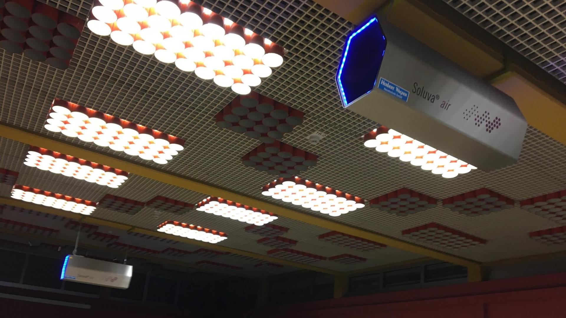 An der Decke eines Klassenzimmers hängt ein sechseckiges silbernes Luftreinigungsgerät. An der Decke eines Klassenzimmers hängt ein sechseckiges silbernes Luftreinigungsgerät.