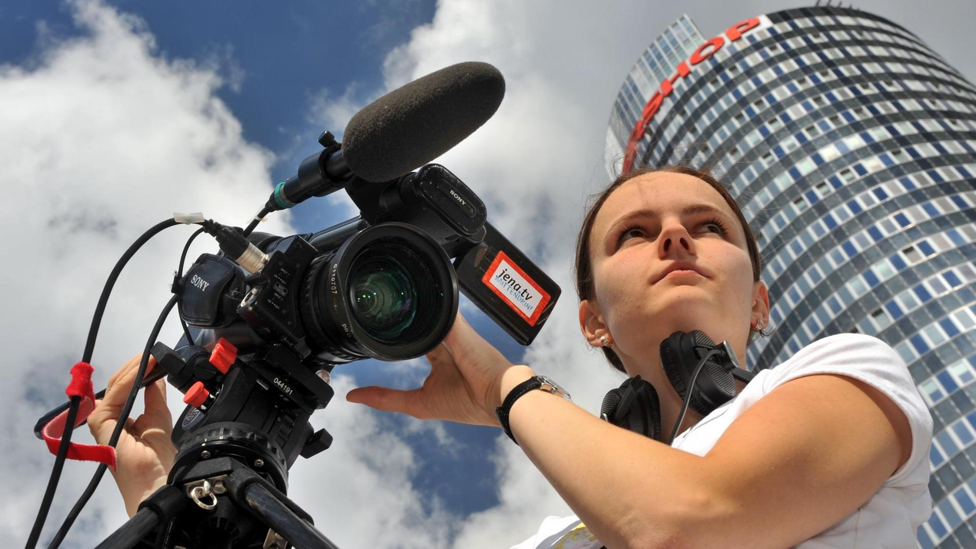 Die Videojournalistin Carolin Stephan von Jena TV richtet in der Jenaer Innenstadt ihre Kamera ein (Foto vom 21.08.2008). Die Redaktionsvolontärin ist eine von derzeit 13 Mitarbeitern des Lokalfernsehsenders. Die Berichterstattung aus der Saalestadt erreicht knapp 40.000 Jenaer Haushalte über das Kabelnetz. In Deutschland sind einer Studie zufolge etwa 190 kommerzielle Anbieter von Lokal-TV lizenziert, rund 70 Prozent davon senden in der ostdeutschen Provinz. Foto: Hendrik Schmidt dpa/lth (zu Korr.-Bericht "Lokale Winzlinge im TV-Markt trotz treuer Zuschauer in Geldnot" vom 24.08.2008) +++(c) dpa - Report+++ | Verwendung weltweit Die Videojournalistin Carolin Stephan von Jena TV richtet in der Jenaer Innenstadt ihre Kamera ein (Foto vom 21.08.2008). Die Redaktionsvolontärin ist eine von derzeit 13 Mitarbeitern des Lokalfernsehsenders. Die Berichterstattung aus der Saalestadt erreicht knapp 40.000 Jenaer Haushalte über das Kabelnetz. In Deutschland sind einer Studie zufolge etwa 190 kommerzielle Anbieter von Lokal-TV lizenziert, rund 70 Prozent davon senden in der ostdeutschen Provinz. Foto: Hendrik Schmidt dpa/lth (zu Korr.-Bericht "Lokale Winzlinge im TV-Markt trotz treuer Zuschauer in Geldnot" vom 24.08.2008) +++(c) dpa - Report+++ | Verwendung weltweit