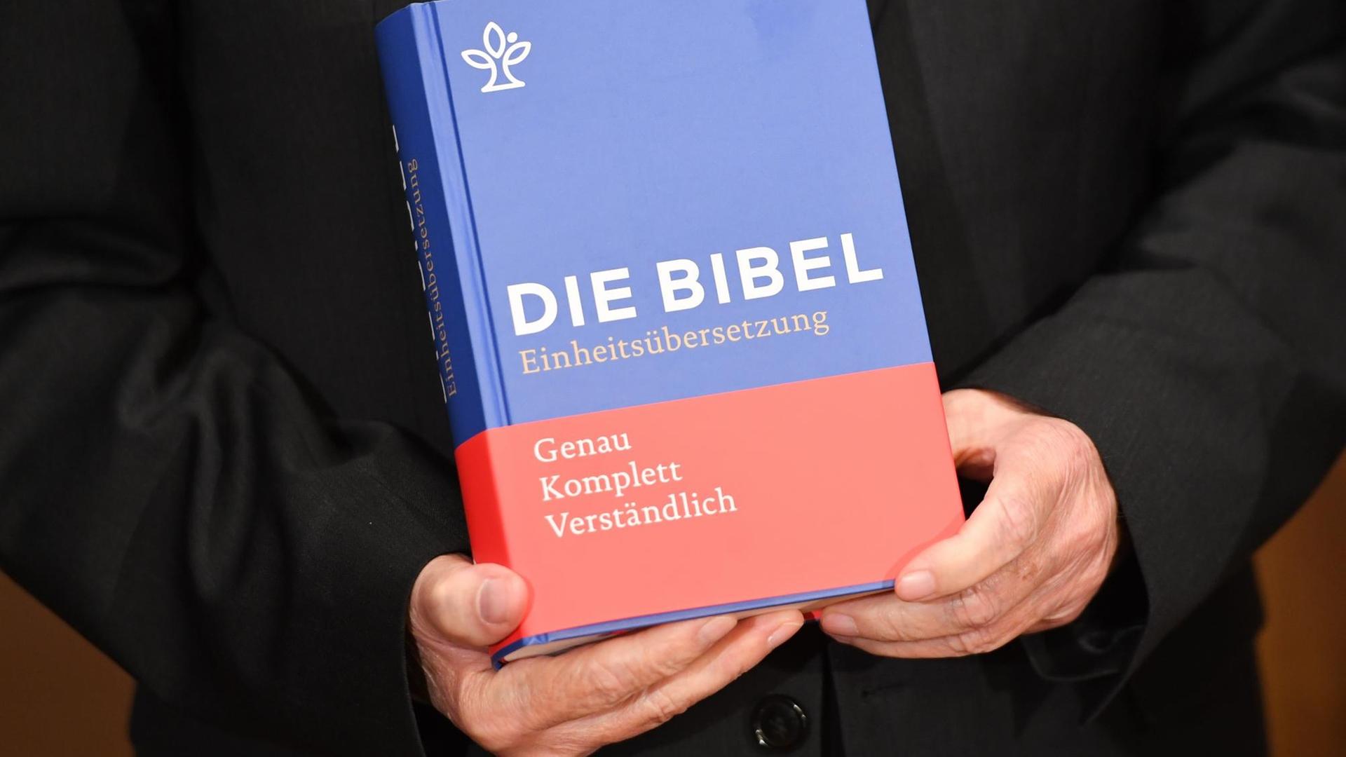 Zwei Hände halten die neue Einheitsübersetzung der Bibel in die Kamera. Zwei Hände halten die neue Einheitsübersetzung der Bibel in die Kamera.