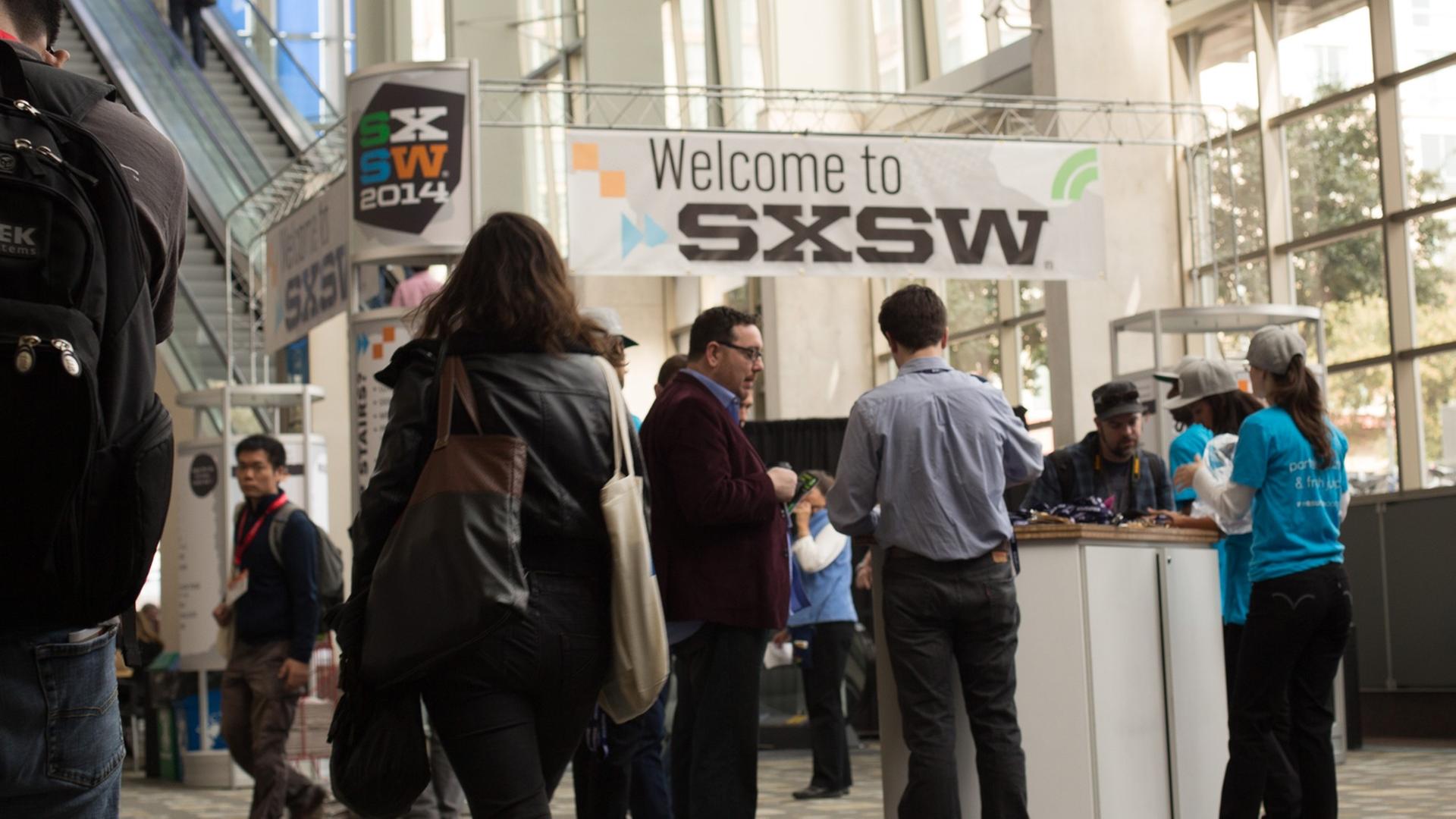 Menschen stehen vor einem Stand auf der Konferenz South by Southwest in Austin. Darüber hängt ein Transparent mit der Aufschrift SXSW. Menschen stehen vor einem Stand auf der Konferenz South by Southwest in Austin. Darüber hängt ein Transparent mit der Aufschrift SXSW.