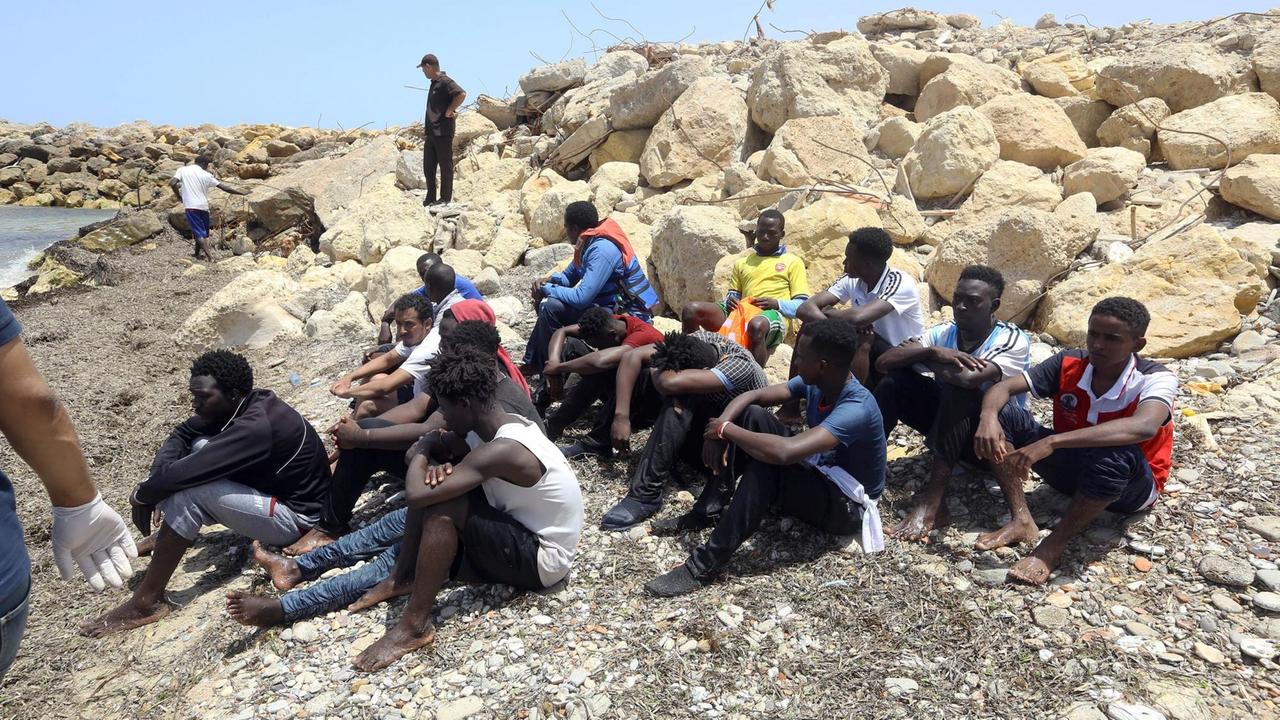 Eine Gruppe von Flüchtlingen sitzt nach einem Schiffsunglück auf Steinen an einem Strand in Libyen.
