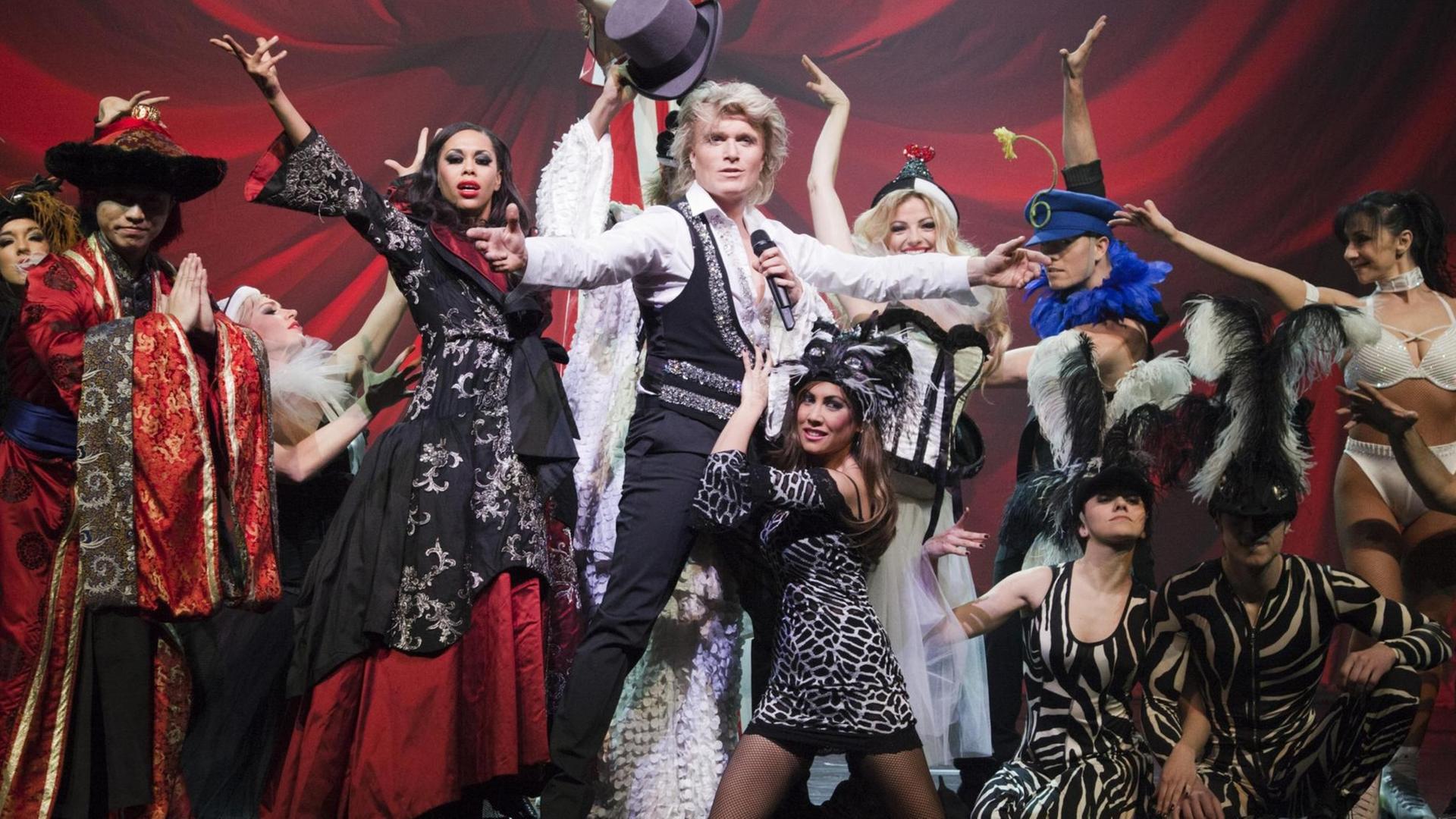 Das Foto zeigt den niederländischen Illusionisten Hans Klok auf der Bühne, umringt von vielen Mitarbeitern. Das Foto zeigt den niederländischen Illusionisten Hans Klok auf der Bühne, umringt von vielen Mitarbeitern.