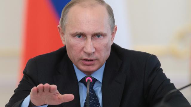 Wladimir Putin sitzt an einem Mikrofon, gestikuliert und spricht