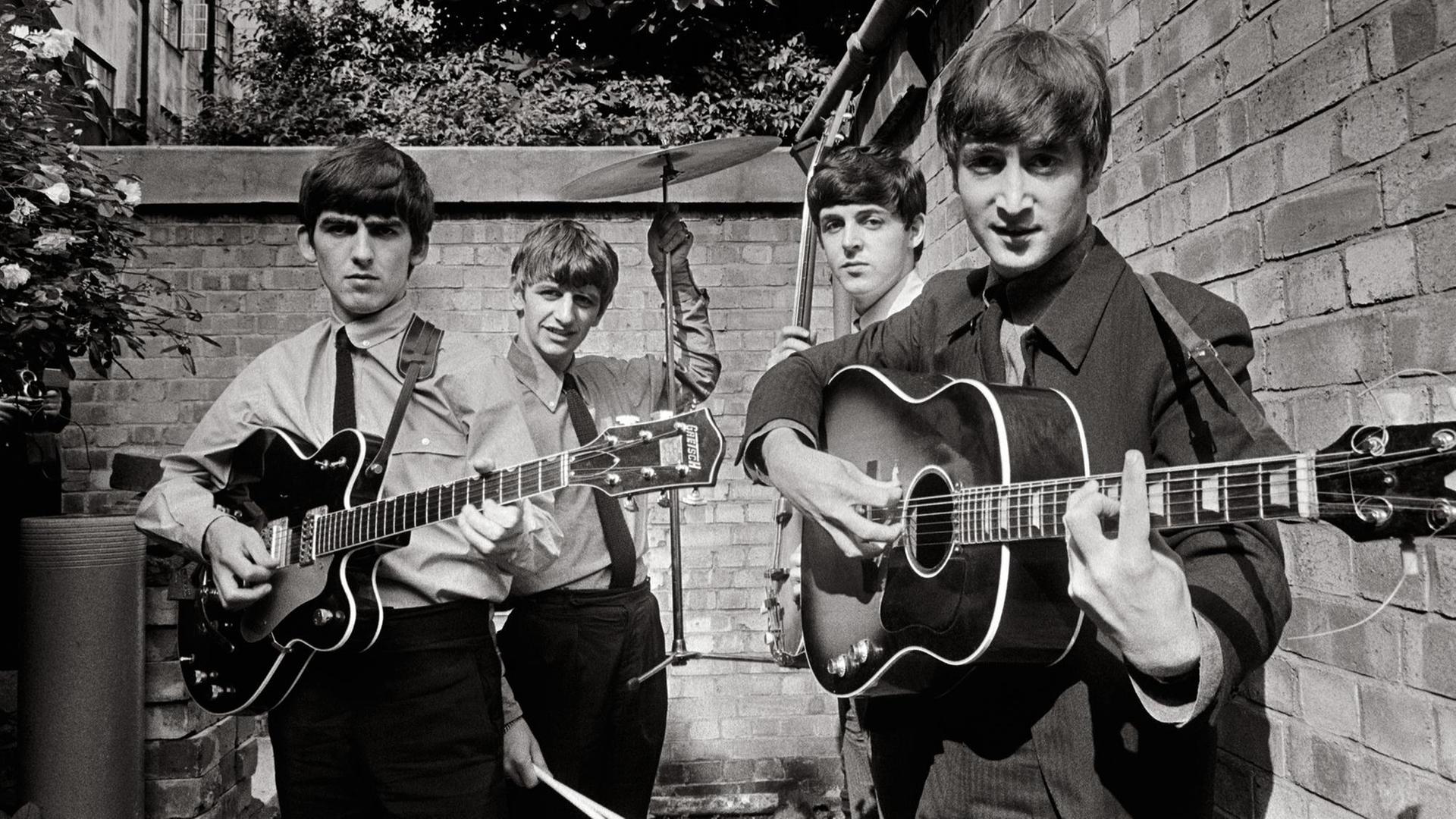 Eine Schwarzweißaufnahme der Beatles mit ihren Instrumenten aus dem Jahr 1963. Zwei stehen vorne, zwei hinten. Eine Schwarzweißaufnahme der Beatles mit ihren Instrumenten aus dem Jahr 1963. Zwei stehen vorne, zwei hinten.