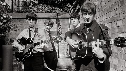 Eine Schwarzweißaufnahme der Beatles mit ihren Instrumenten aus dem Jahr 1963. Zwei stehen vorne, zwei hinten. 