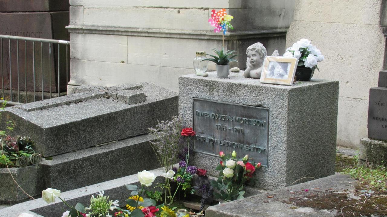 Ein Grab mit einem mittelhohen rechteckigen Grabstein, auf dem ein Foto des Sängers, Ein steinerner Engelskopf und ein buntes Windrad stehen. Auf dem Grab wachsen einige weiße und rote Rosen. Ein Grab mit einem mittelhohen rechteckigen Grabstein, auf dem ein Foto des Sängers, Ein steinerner Engelskopf und ein buntes Windrad stehen. Auf dem Grab wachsen einige weiße und rote Rosen.