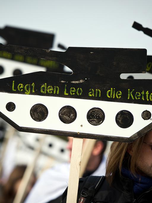 Ein Demonstrant trägt ein Schild in Form eines Panzers aus Holz mit der Aufschrift "Legt den Leo an die Kette"