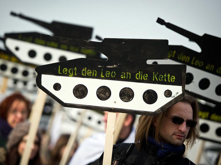 Ein Demonstrant trägt ein Schild in Form eines Panzers aus Holz mit der Aufschrift "Legt den Leo an die Kette"