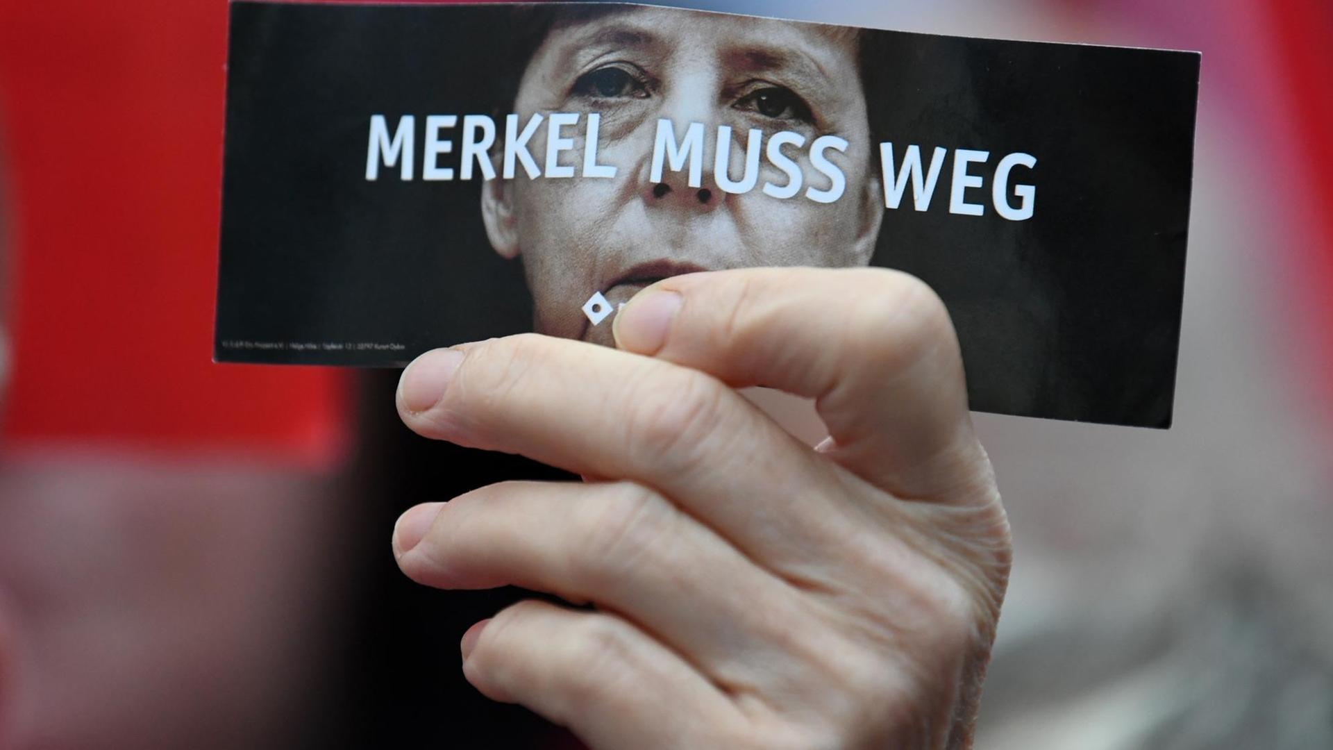 Demonstranten protestieren in Finsterwalde während einer Wahlkampfveranstaltung der CDU auf dem Marktplatz gegen Bundeskanzlerin Angela Merkel. Ein Demonstrant hält eine Karte mit der Aufschrift "Merkel muss weg".