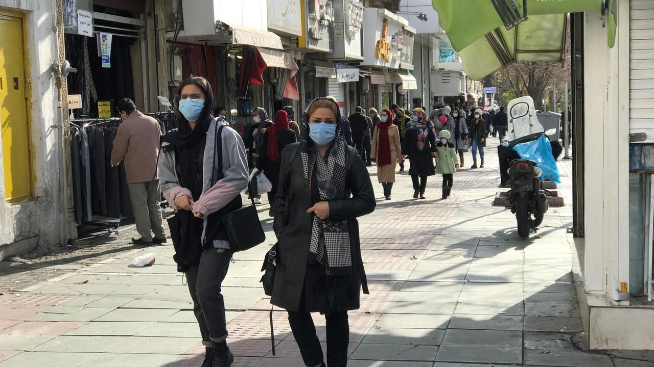 Zwei Frauen mit hellblauem Mundschutz schlendern durch die sonnige Fußgängerzone von Teheran. Zwei Frauen mit hellblauem Mundschutz schlendern durch die sonnige Fußgängerzone von Teheran.