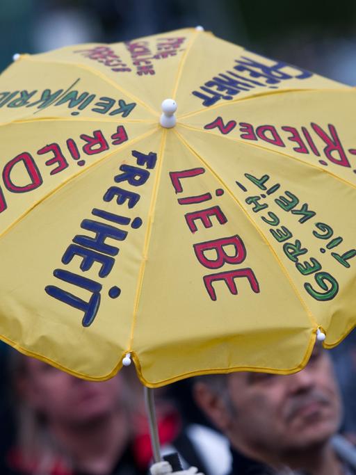 Ein Teilnehmer der Montagsdemo am 12.05.2014 in Berlin hält einen Regenschirm mit der Aufschrift "Liebe, Freiheit, Gerechtigkeit" hoch.