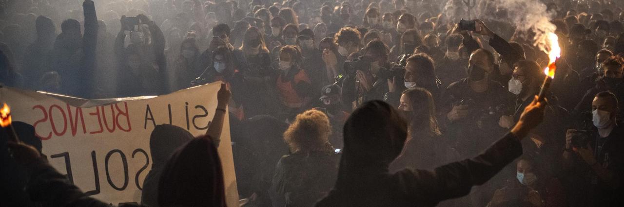 In Barcelona versammeln sich Demonstrierende bei Protesten gegen die Einschränkungen des öffentlichen Lebens wegen der Corona-Pandemie. Es ist dunkel, ein Mann hält eine Fackel hoch. In Barcelona versammeln sich Demonstrierende bei Protesten gegen die Einschränkungen des öffentlichen Lebens wegen der Corona-Pandemie. Es ist dunkel, ein Mann hält eine Fackel hoch.