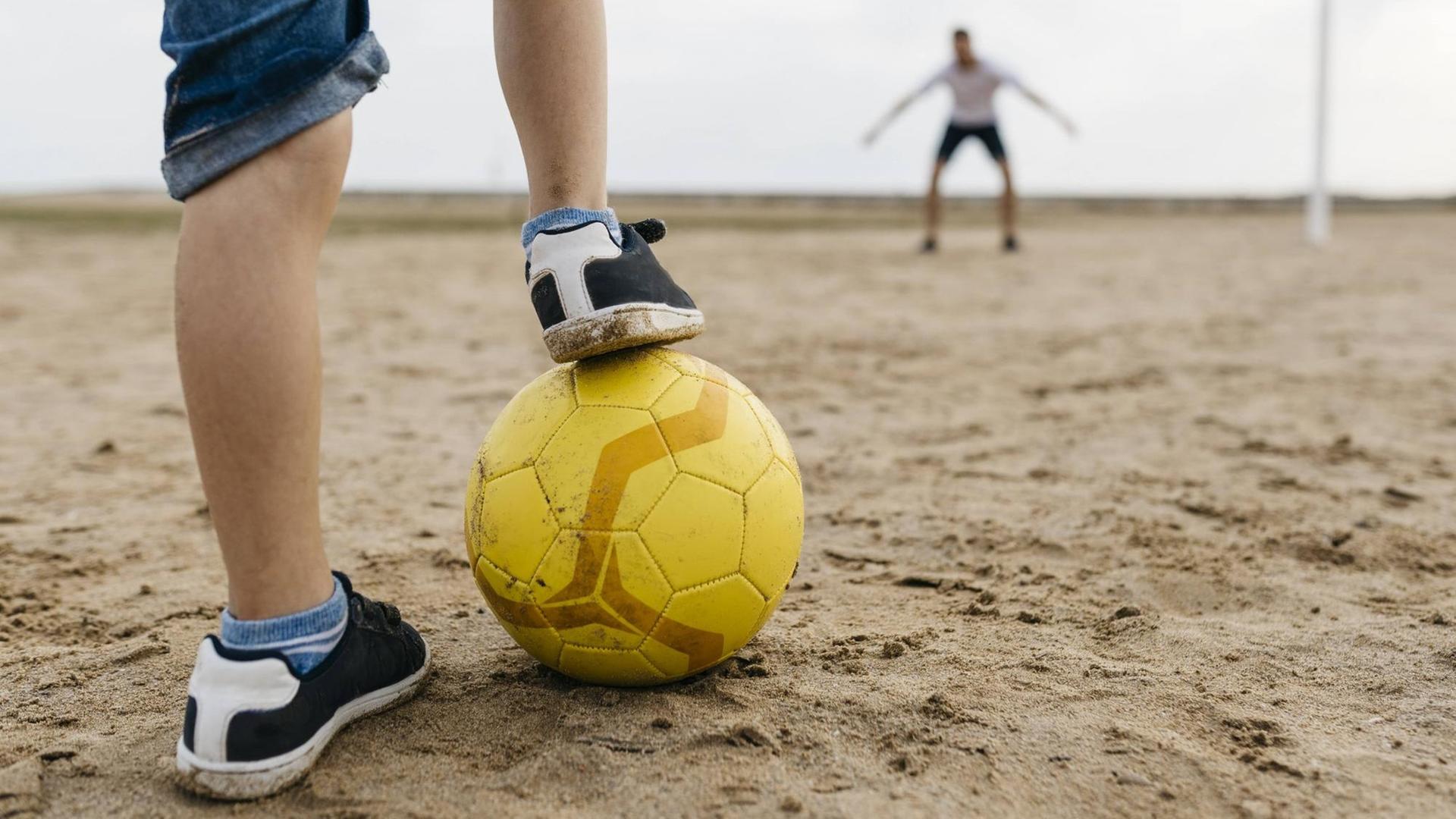 Die Beine eines Jungen mit Fußball, vor einem Tor mit Torwart Die Beine eines Jungen mit Fußball, vor einem Tor mit Torwart