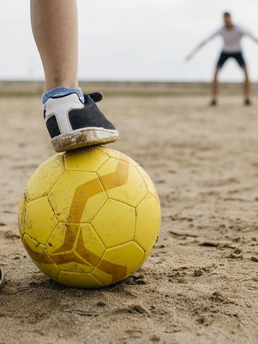 Die Beine eines Jungen mit Fußball, vor einem Tor mit Torwart